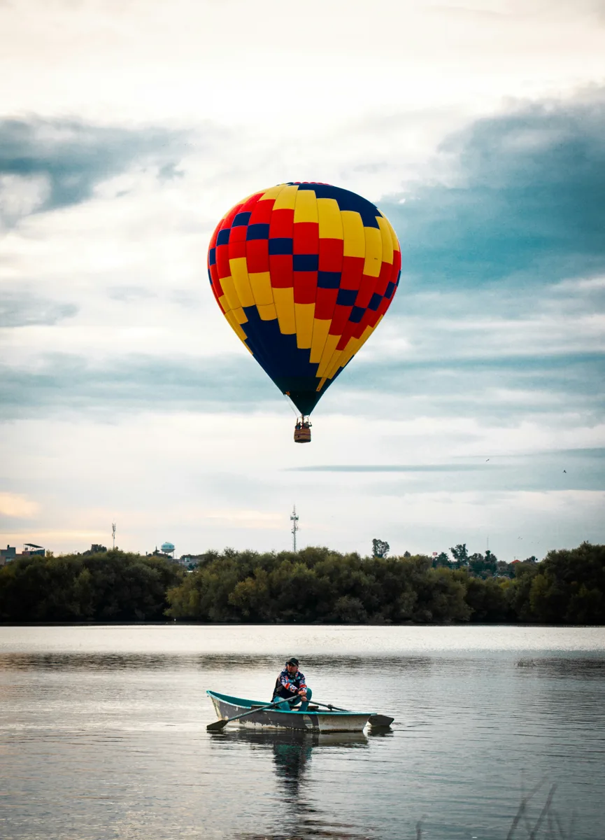 hot air balloon over a lake with a person on a boat in the middle of the lake.