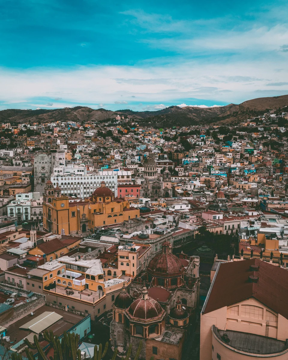 view of guanajuato from above with an orange and red church below and a blue sky above the city.