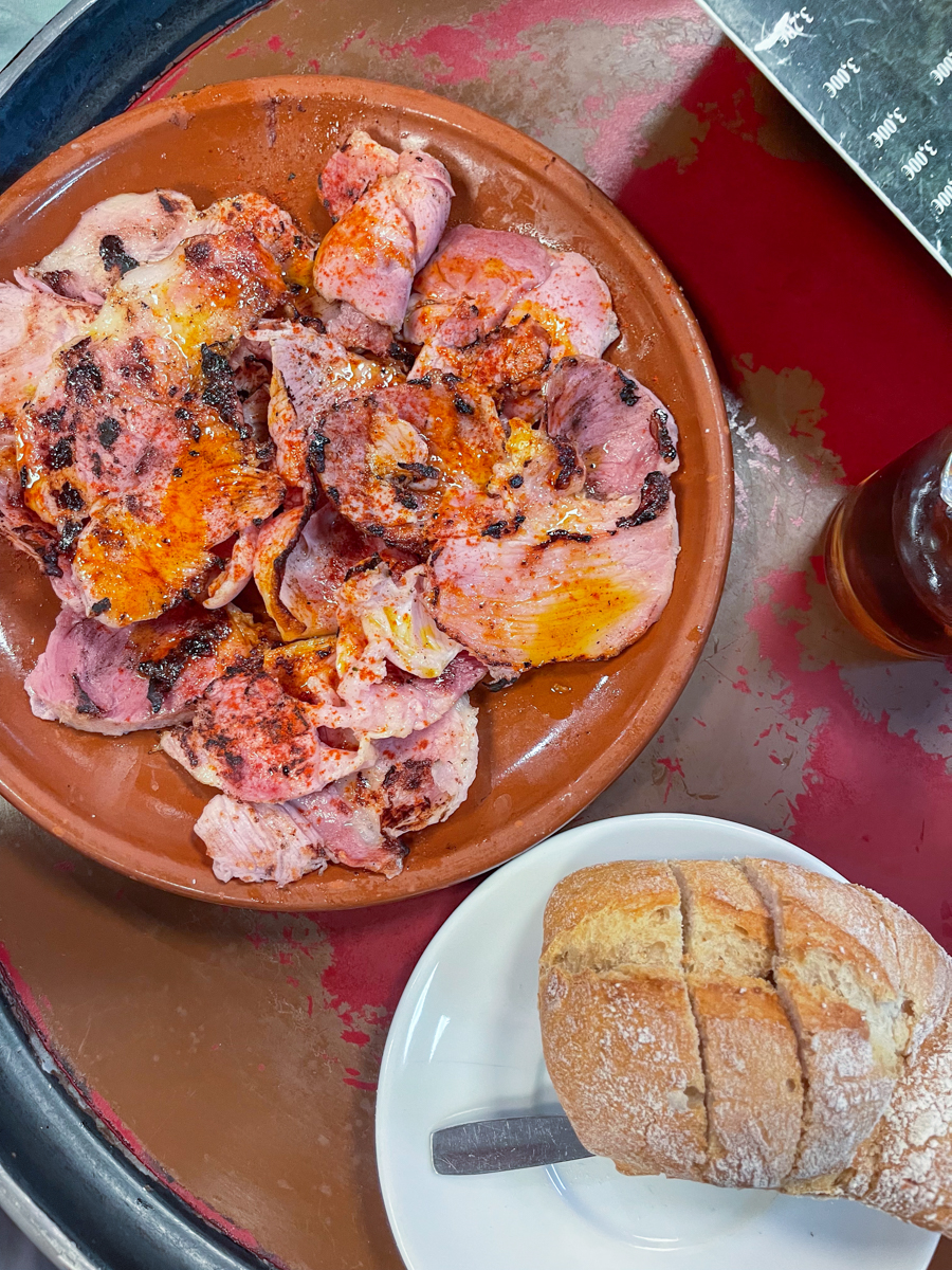 plate of grilled sliced ham in a terracotta dish next to a white plate with sliced baguette bread on it.