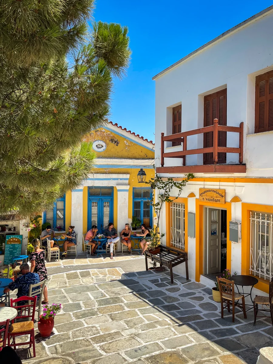 Greek town with restaurant and people sitting outside of it.