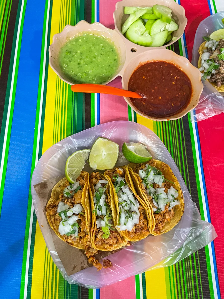 plate of four tacos packed full of meat and onions and on the side are green and red salsas.