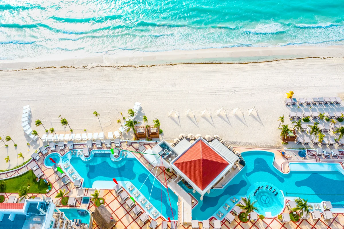 above an all inclusive resort with pools and the beach and ocean next to it.