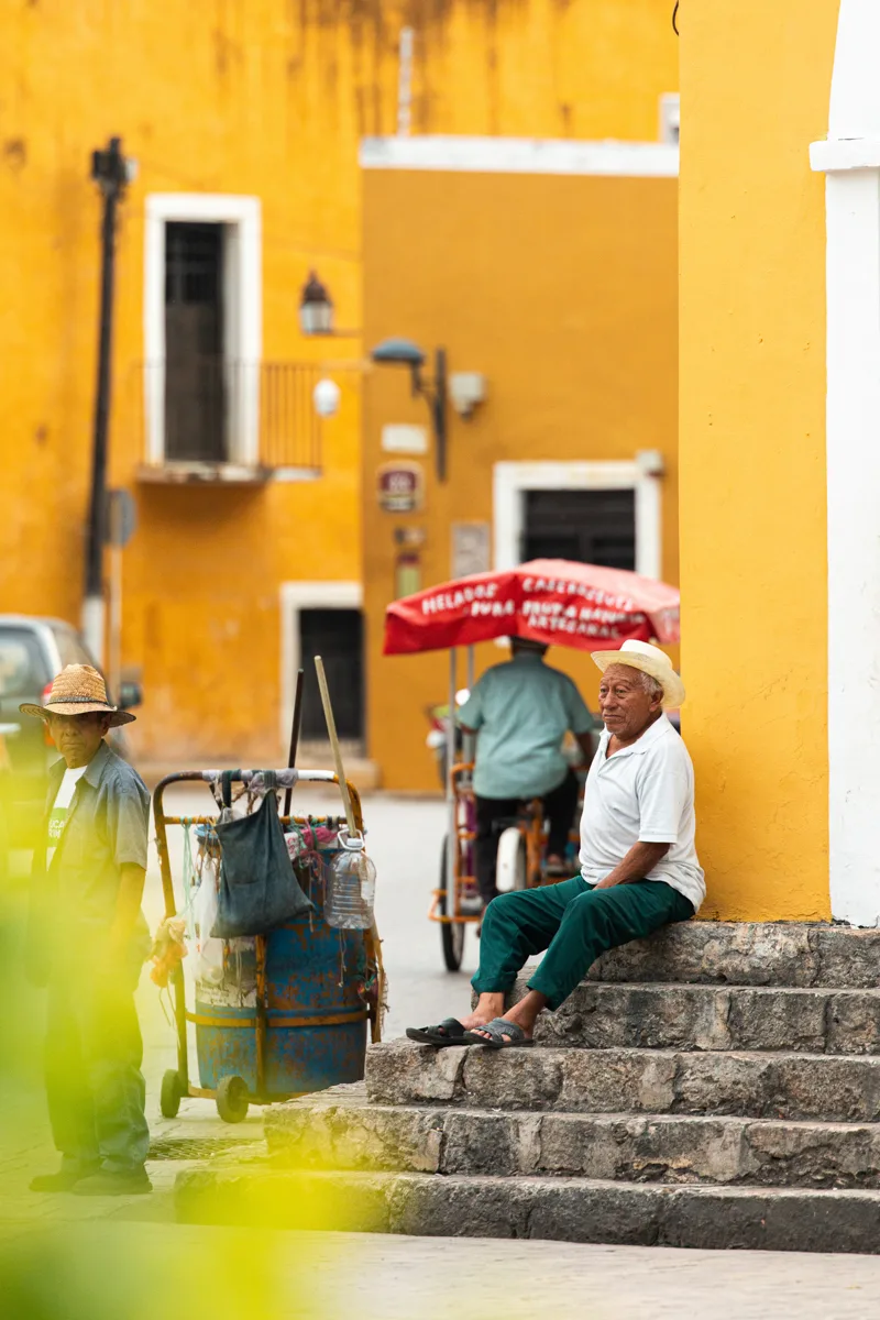 yucatan magic town of izamal with yellow buildings and two people sitting outside on steps.