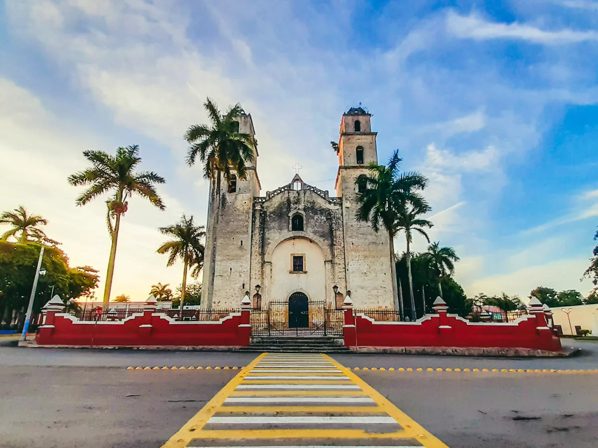church with two towers at the front with palm trees and a long yellow crosswalk that leads to the entrance.