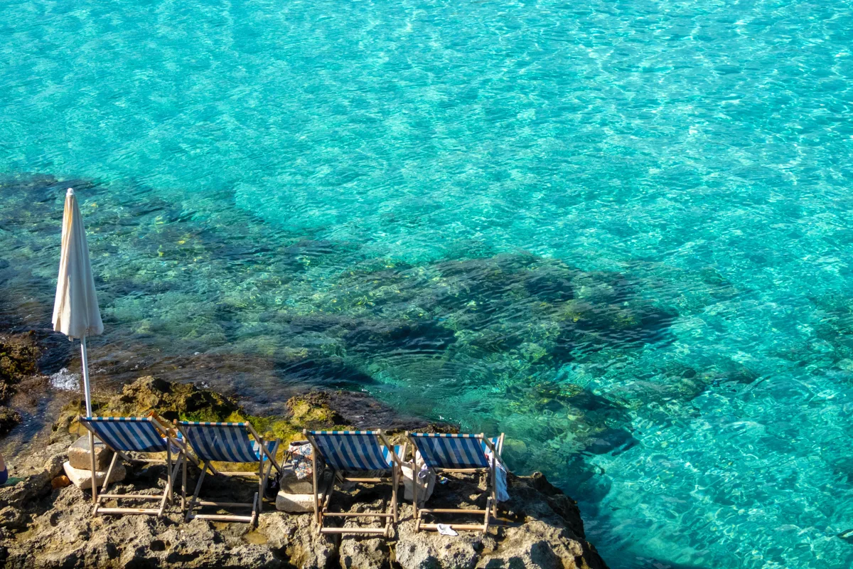 chairs on rocks with turquoise water in front of them.