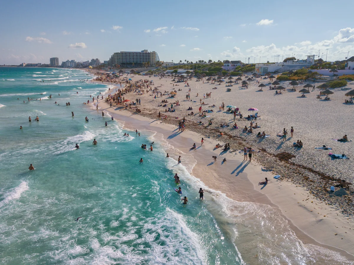 busy beach with people swimming and laying on the sand.