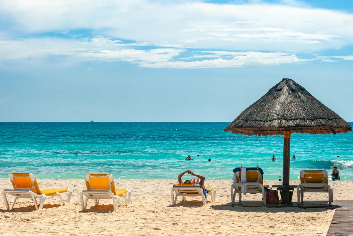 turquoise waters with empty chairs and a palapa umbrella on the beach.