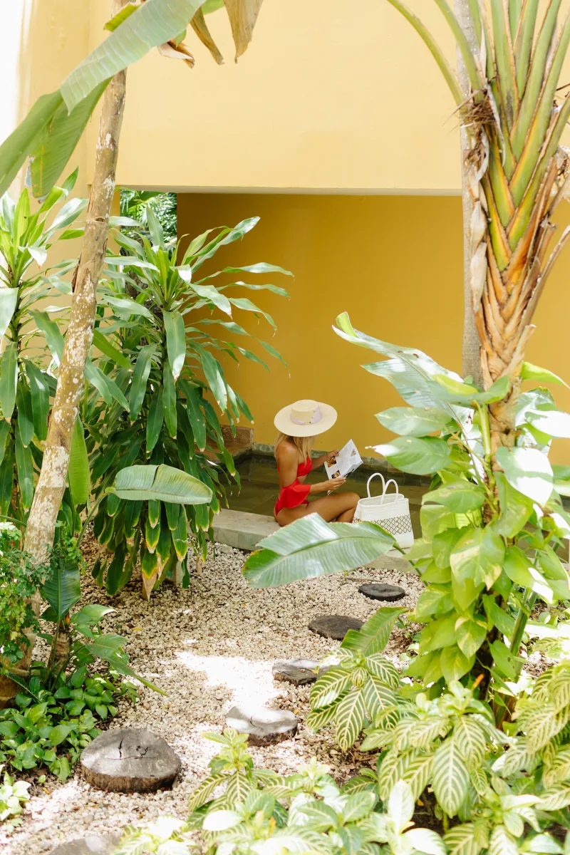 woman reading in a garden with a yellow building behind her.