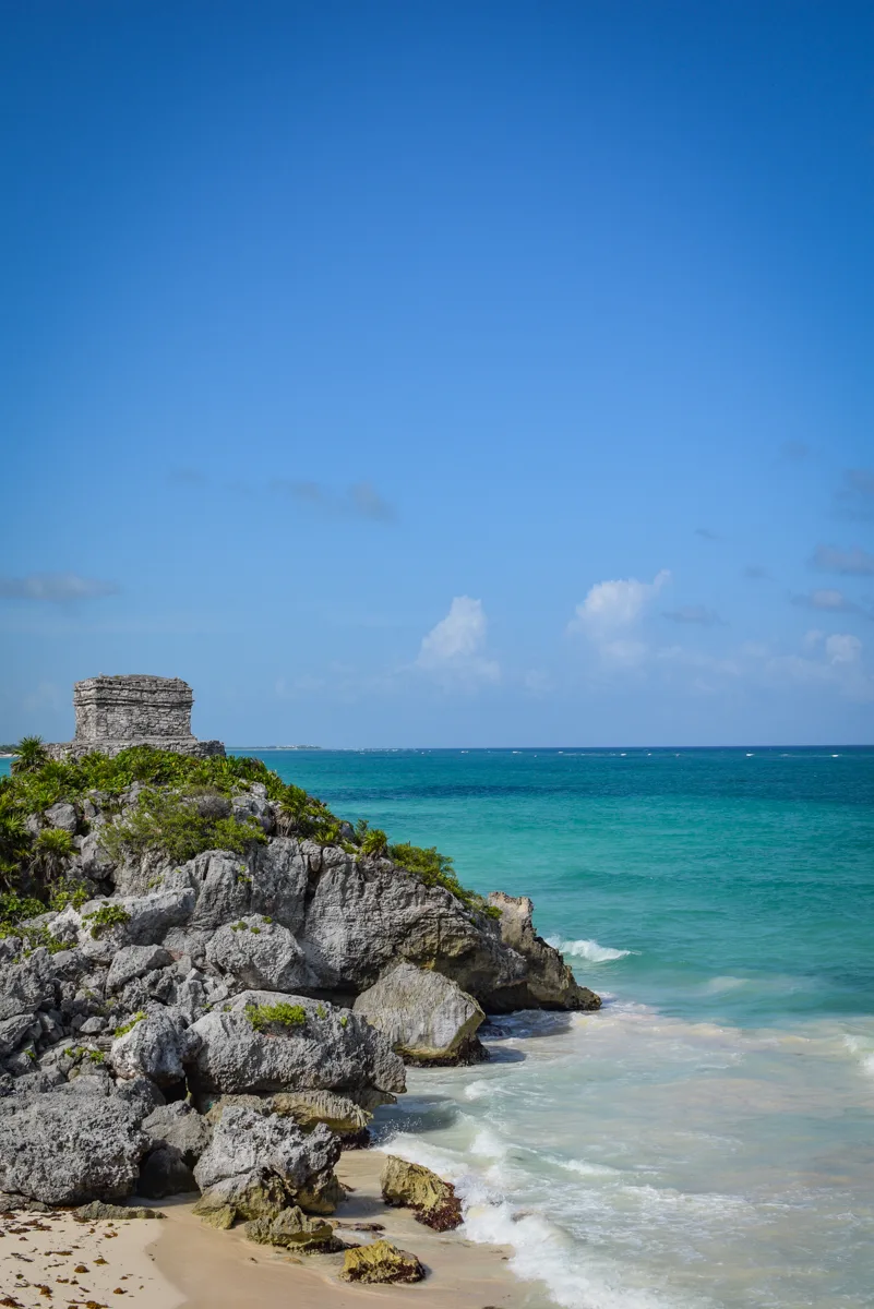 tulum archaeological site with ruins on the cluffs and turquoise waters on the beach below.
