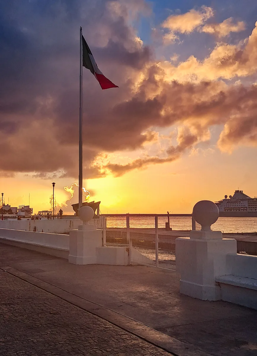 sun setting with the mexican flag overhead near the port in cozumel.
