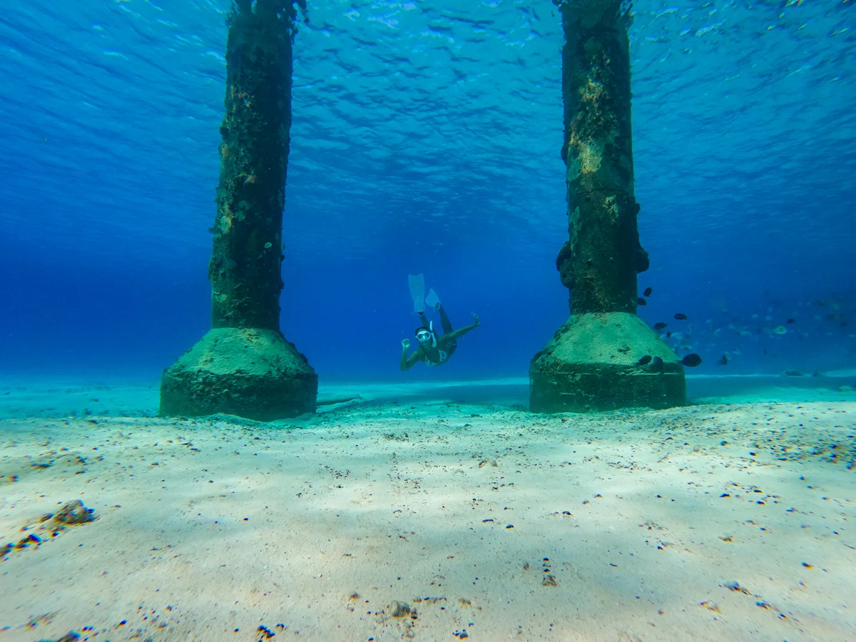 woman swimming underwater between two pillars, one of the best things to do in cozumel.