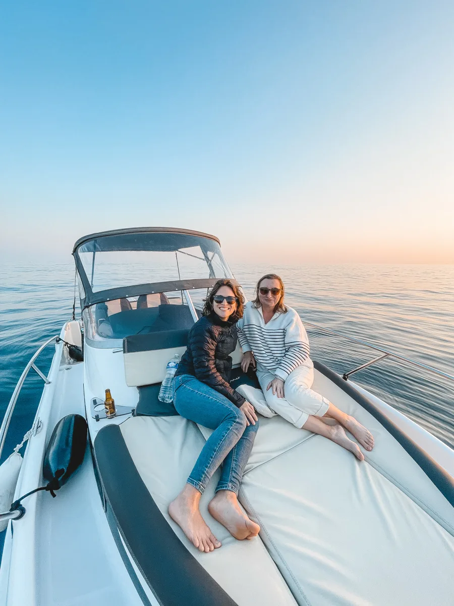 two women sitting on a boat with the sun setting behind them.