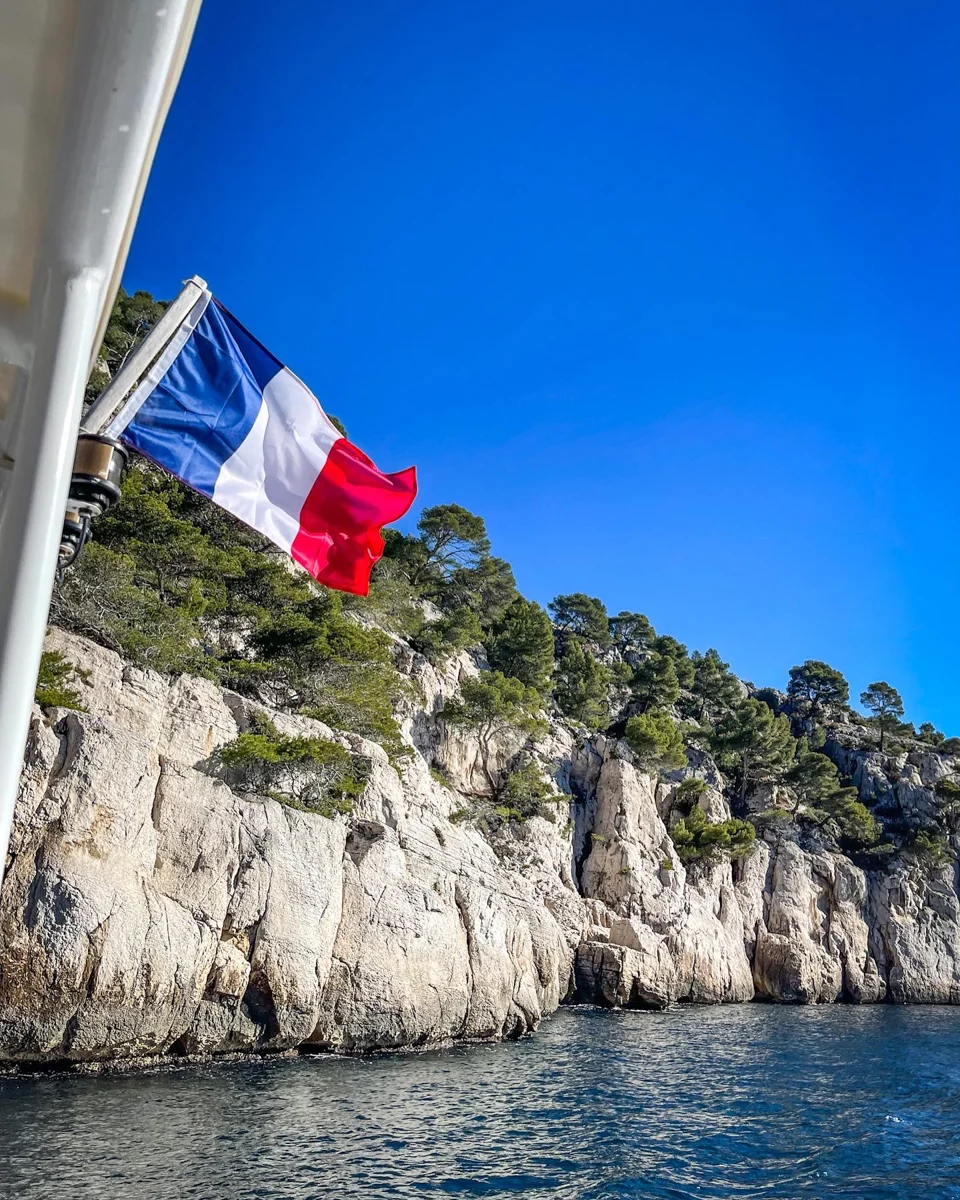flag of france on the back of a boat with the calanques of Cassis in the background.
