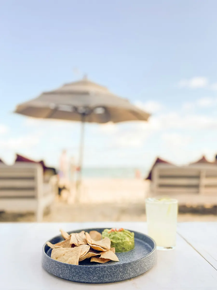 plate of guacamole and chips on a table at the beach with umbrellas and chairs in front of the table.