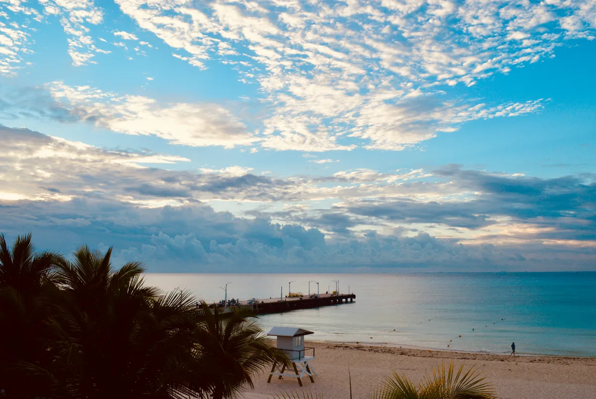beach views with white puffy clouds in the sky and a flat caribbean sea in the background.