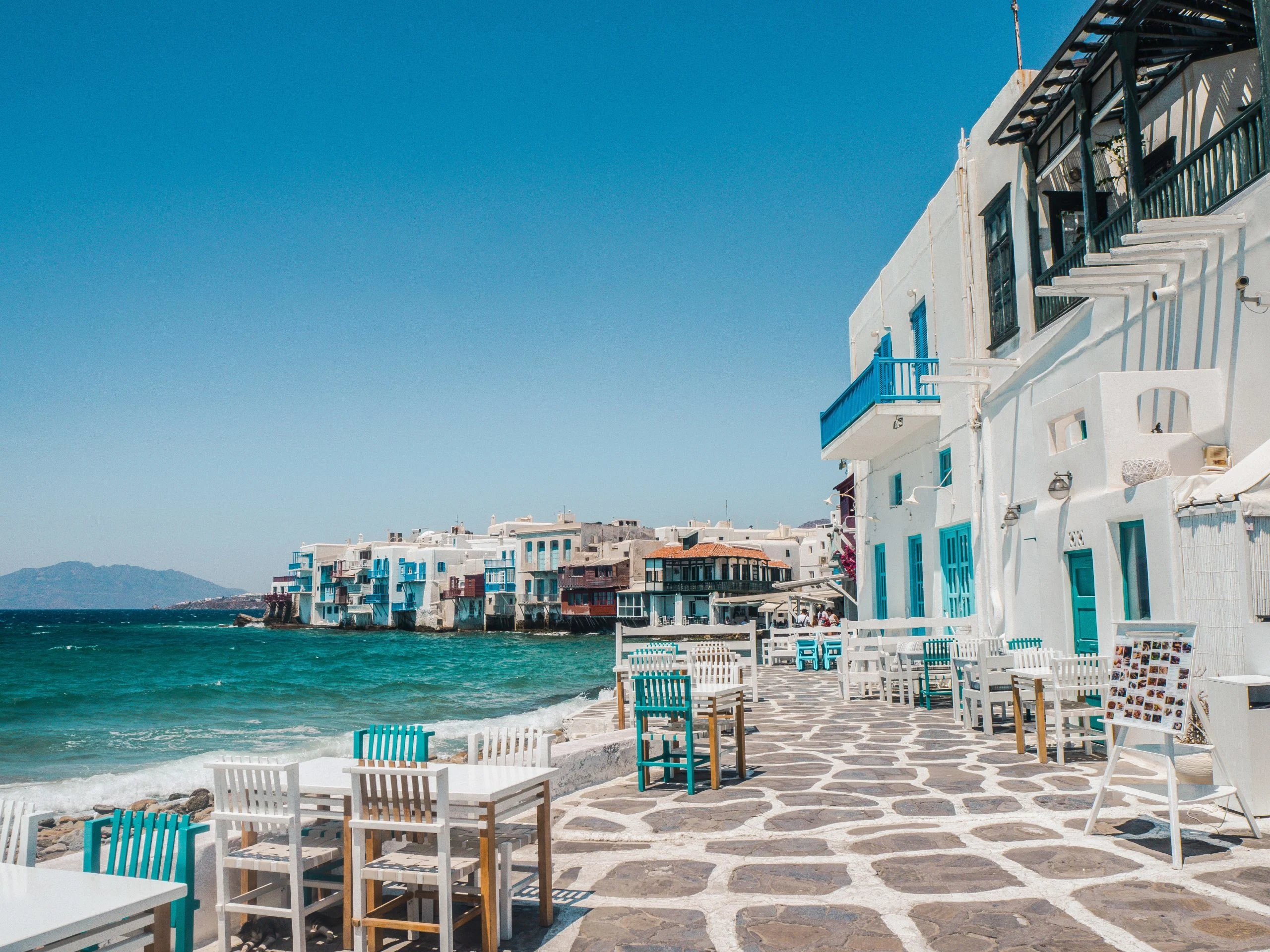what to pack for europe in summer is easy when you are visiting a greek island like this with warm weather, white washed buildings, turquoise seas and tables to dine al fresco.