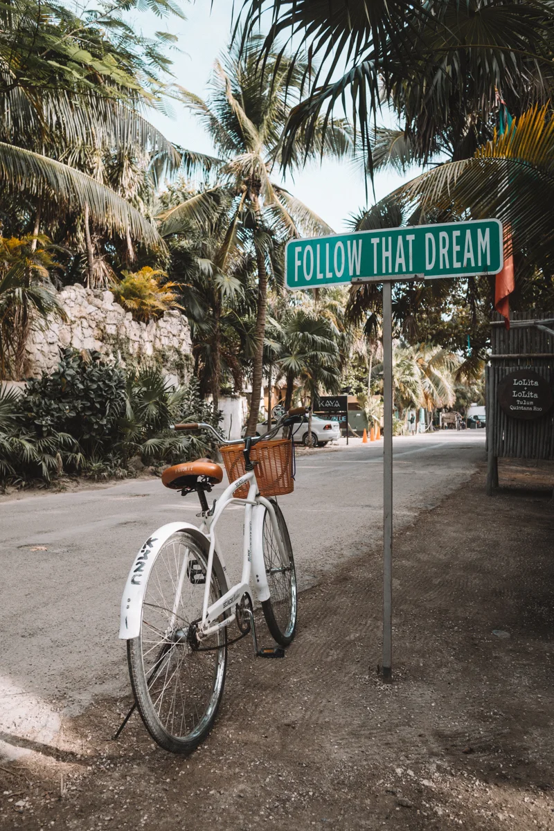 bicycle on the side of the road with a sign that says follow your dreams in the beach area of Tulum.