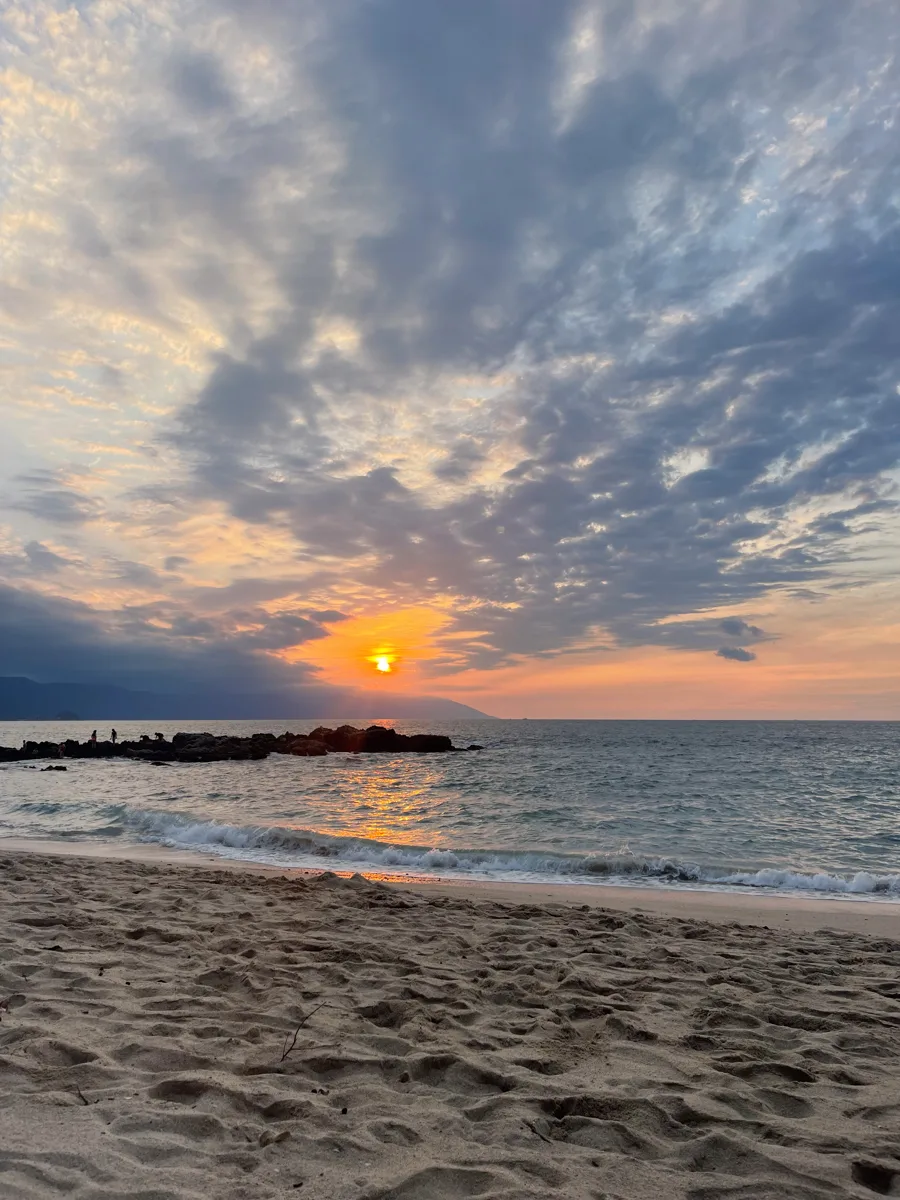 sunset over the ocean with the sand of the beach in the foreground.
