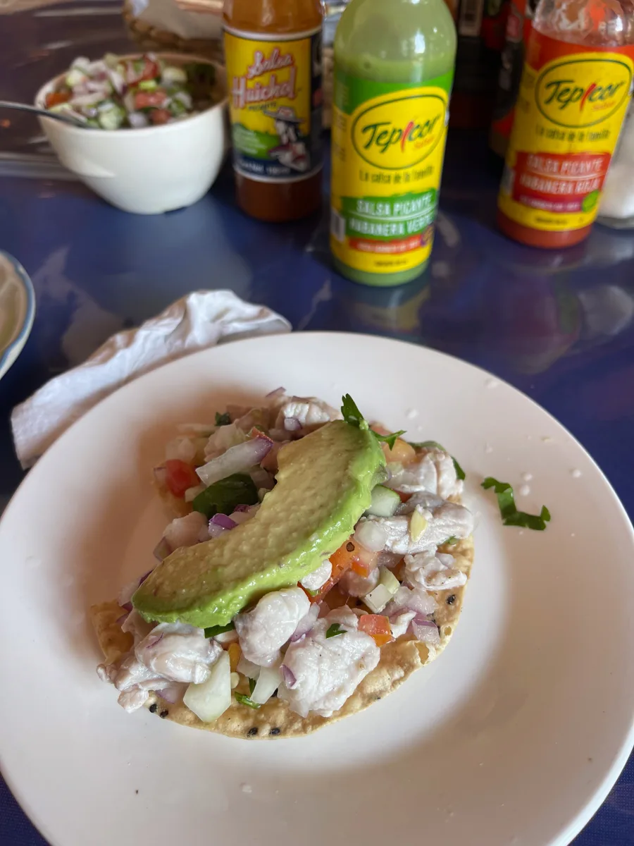 ceviche on a tostada on a white plate with salsas in the background.