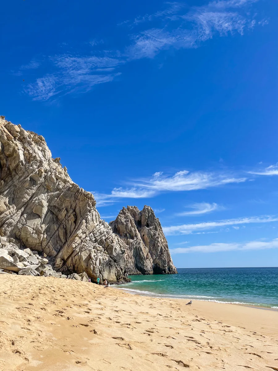 Beach with rock formations in the background and bright blue water in the forground.
