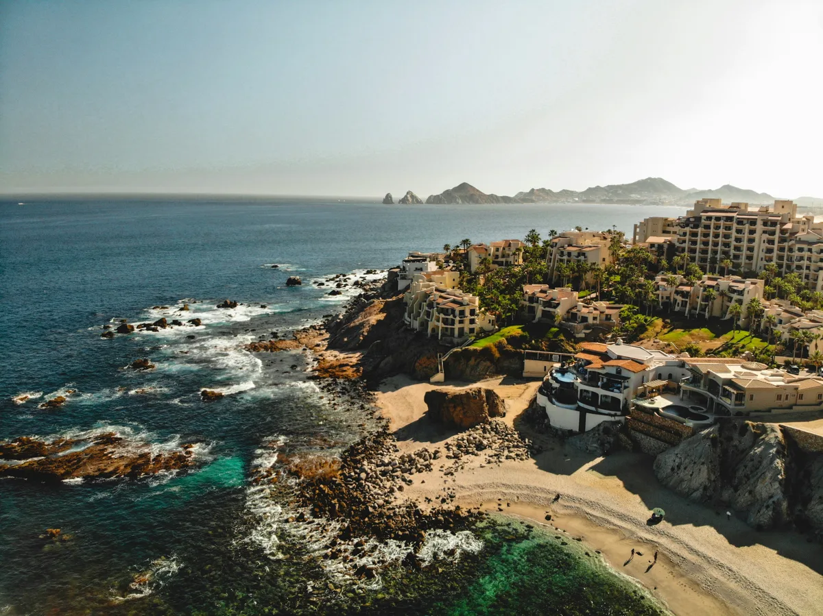 cabo san lucas beaches with an aerial view from above and hotels scattered across the land and dark blue ocean to the left.