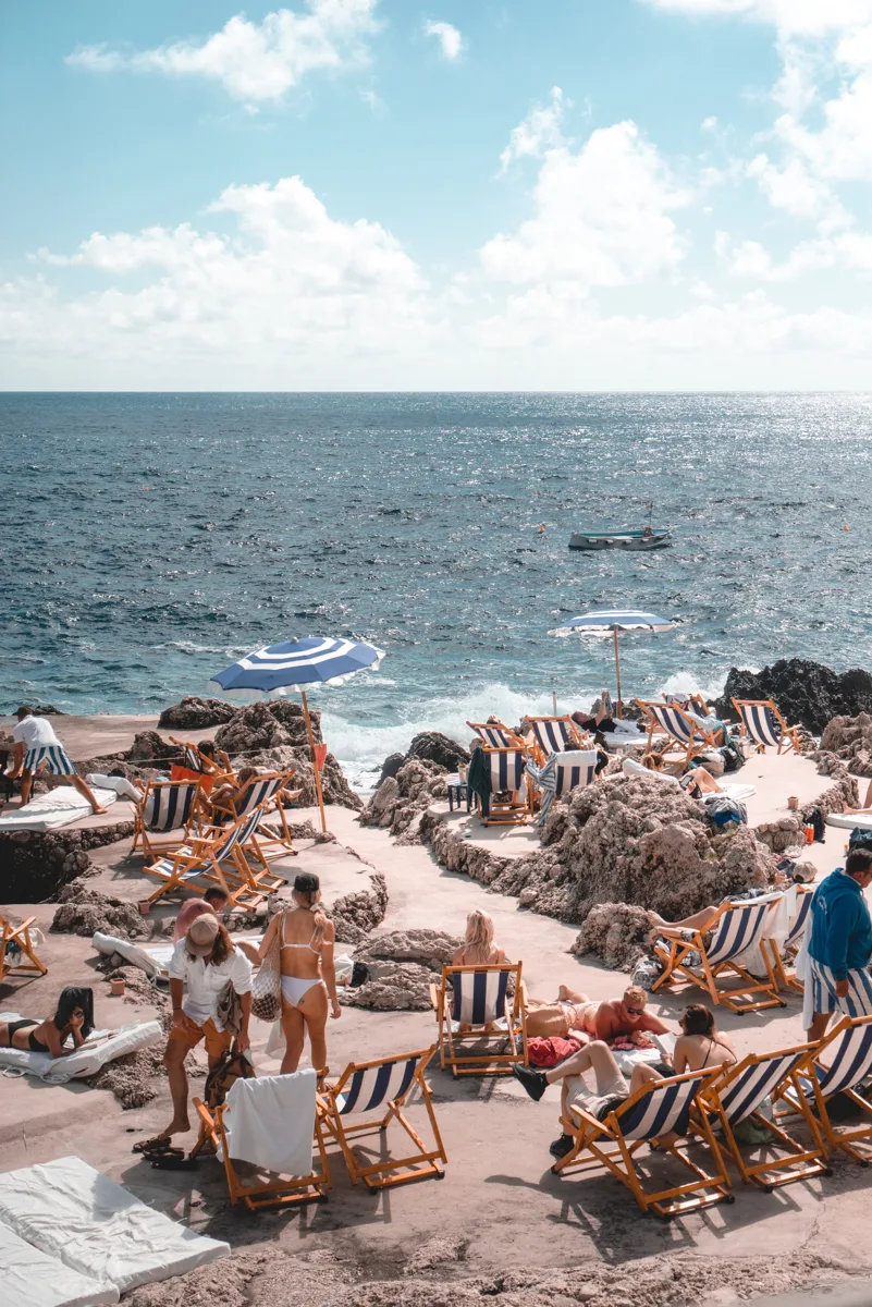 beach with people relaxing in chairs and the sea in the background in Capri, one of the best day trips from Naples.