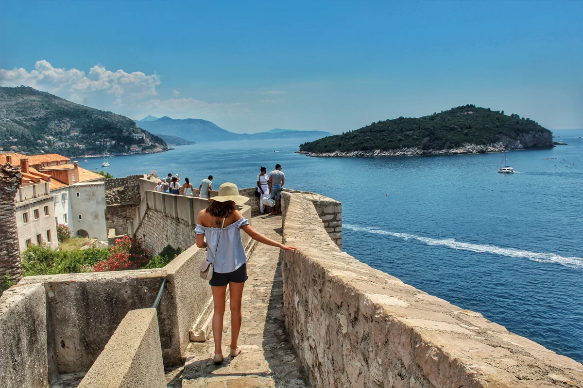 woman walking out on a waterfront walkway made of stone with an island in the distance.
