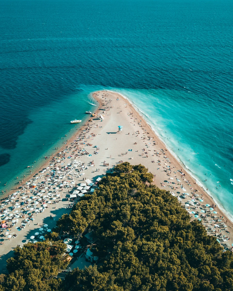 beach shaped like a triangle with dark deep water and land that is bordered by white sand beach with green trees in the middle of the land mass.
