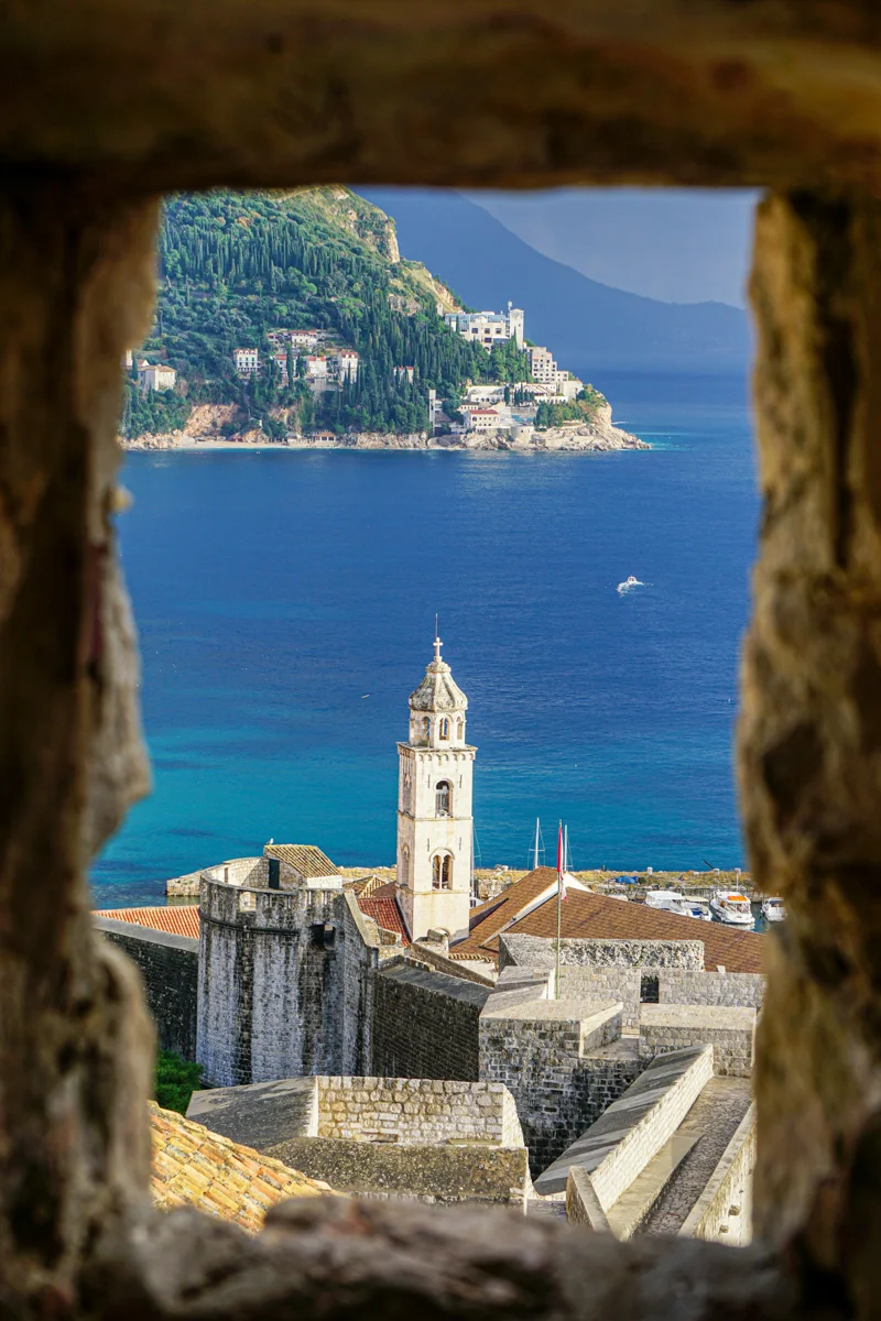view of a city below from a castle window with bright blue water behind the city.