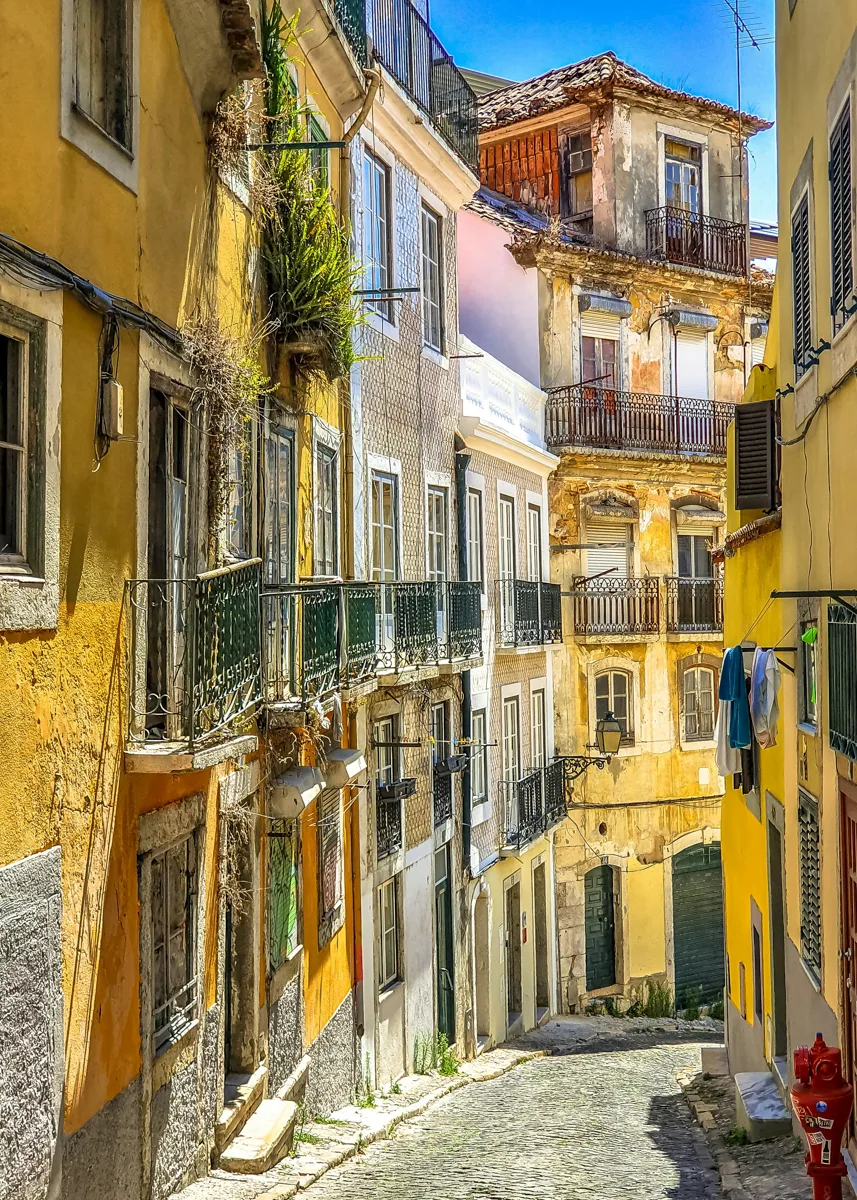 alleyway with bright yellow buildings on both sides and balconies on the second level with bright blue skies above.
