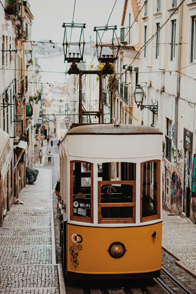white and yellow tram going up a hill on a cobbled street in Lisbon, portugal.