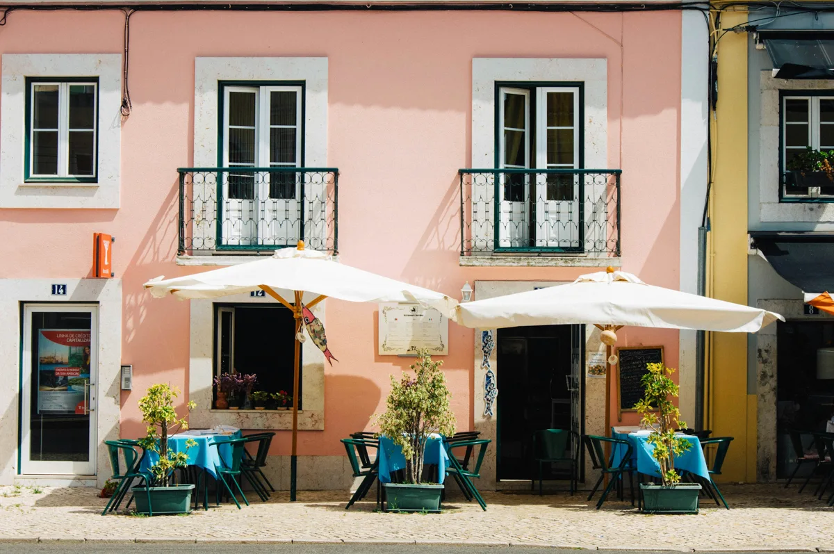 peach building with two umbrellas and three tables outside in the sunshine.