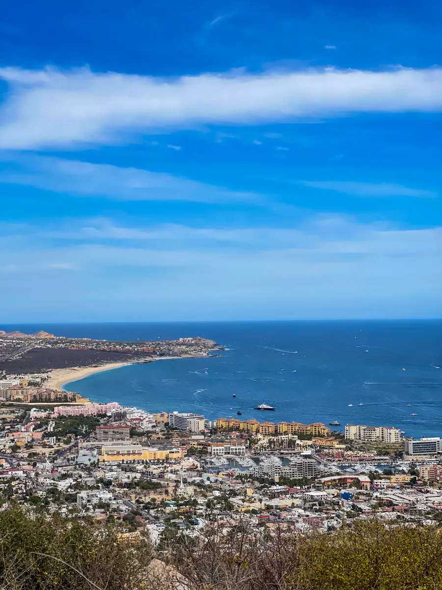 cabo san lucas from above with city sprawled out below and a crescent shaped bay next to the ocean.