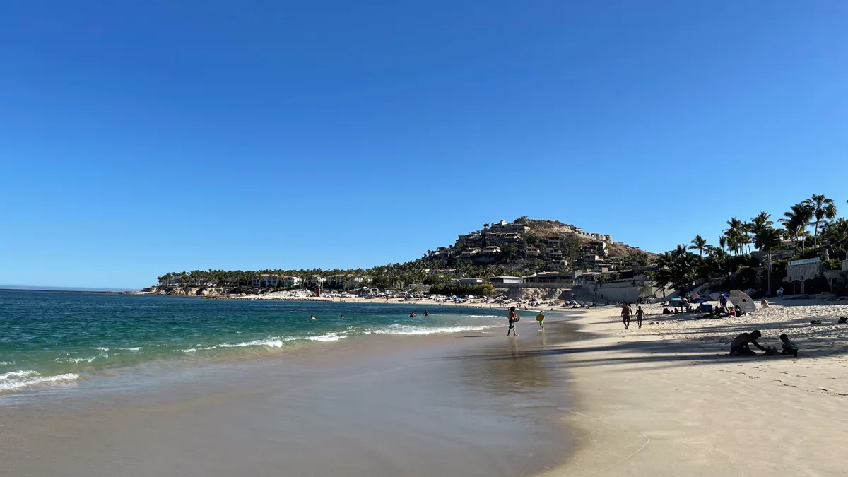 beach in san jose del cabo with ocean to the right, sand to the left, and hills at the end of the sand.