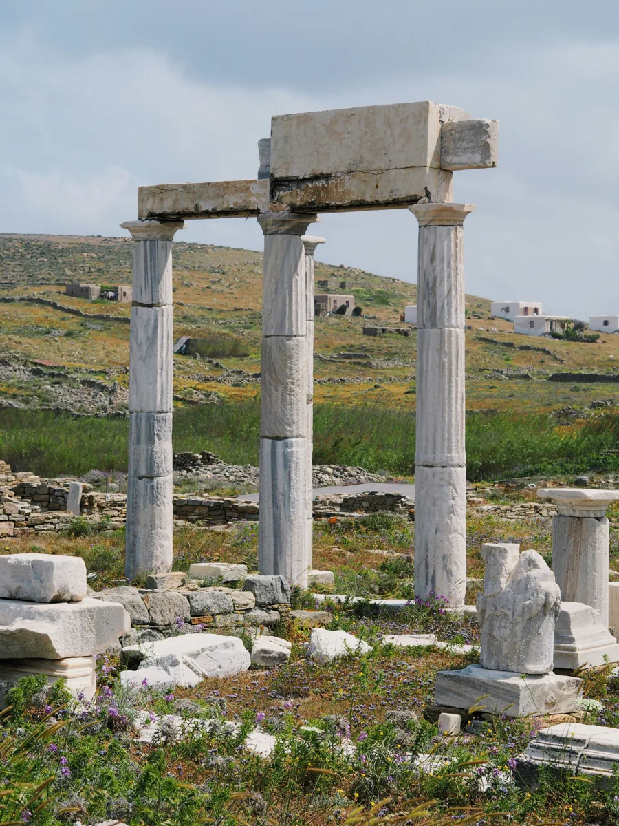 greek ruins with marble pilars standing in a row with pieces of stone on the ground around them.