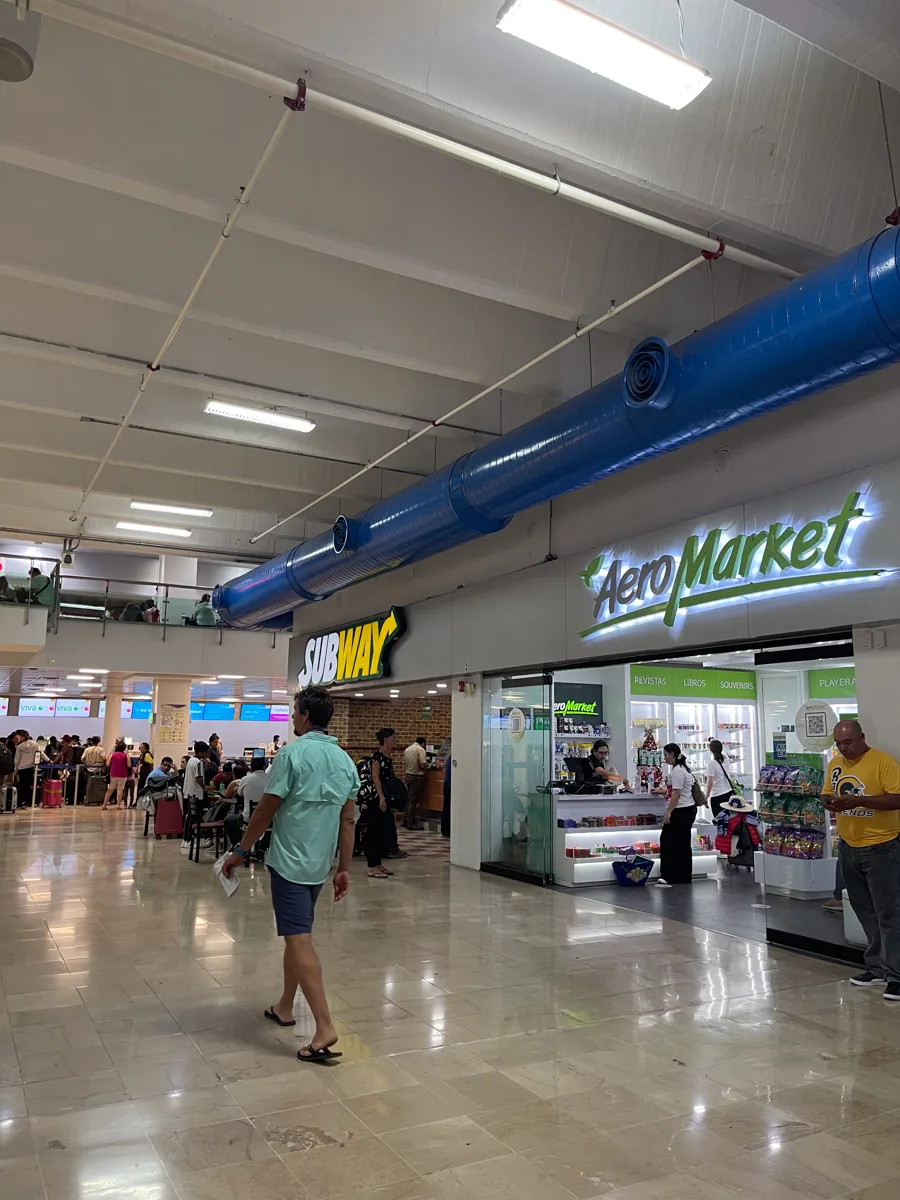 inside of the airport with Subway and Aeromarket and people walking around.