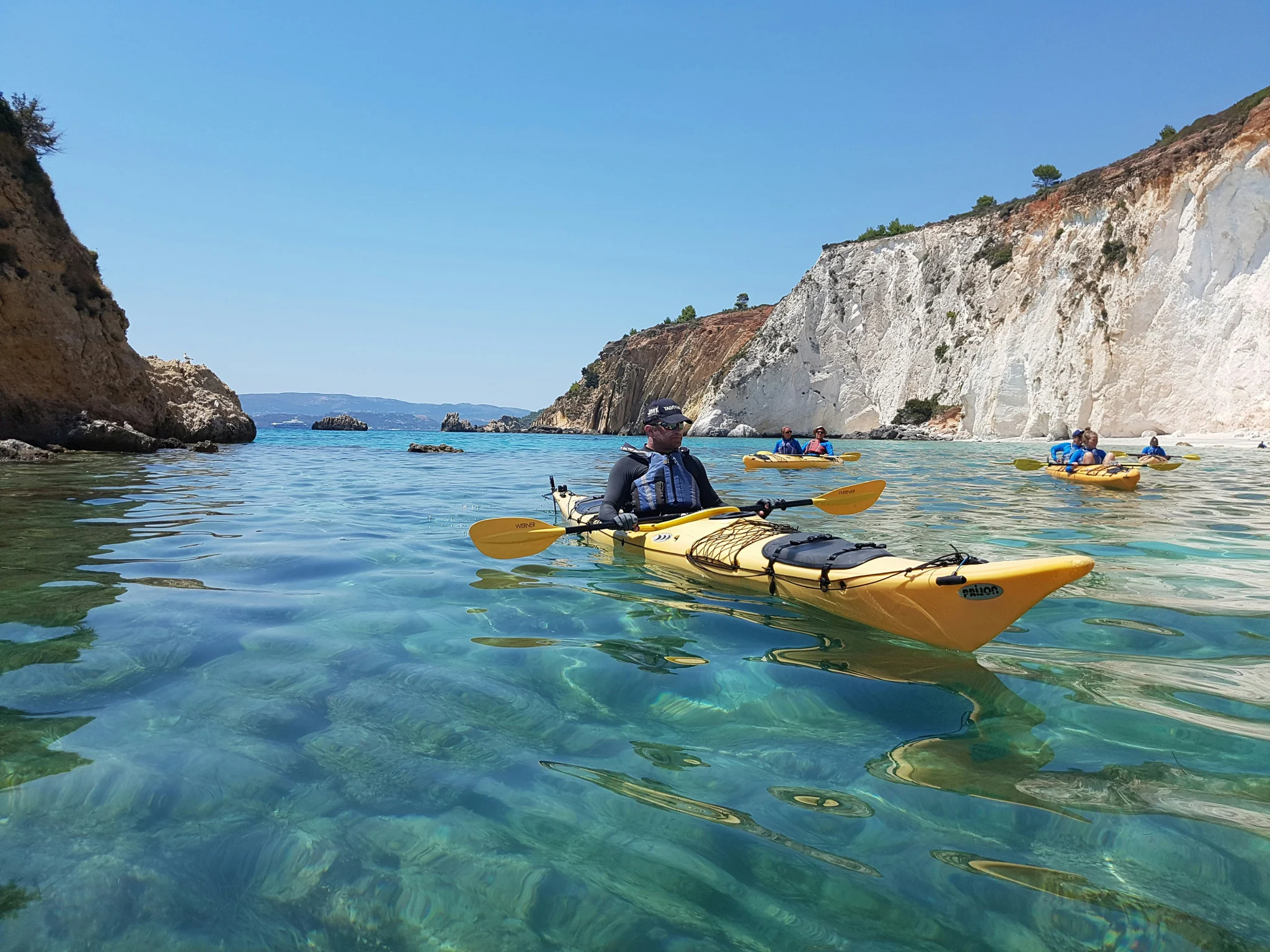 person in a yellow kayak in clear turquoise water with white cliffs behind them at one of the most beautiful beaches in Kefalonia Greece.