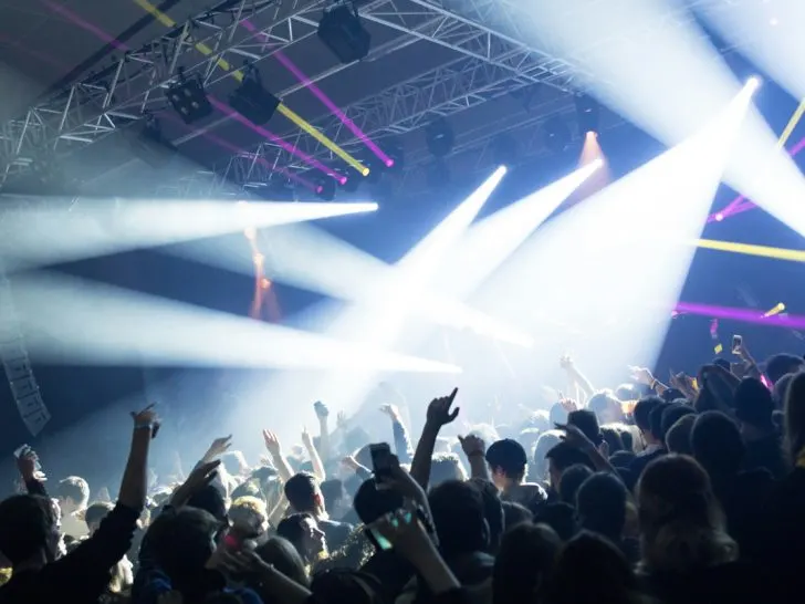 cancun nightlife with a dance club that has a stage at the front and light beams coming from different directions all into the crowd.