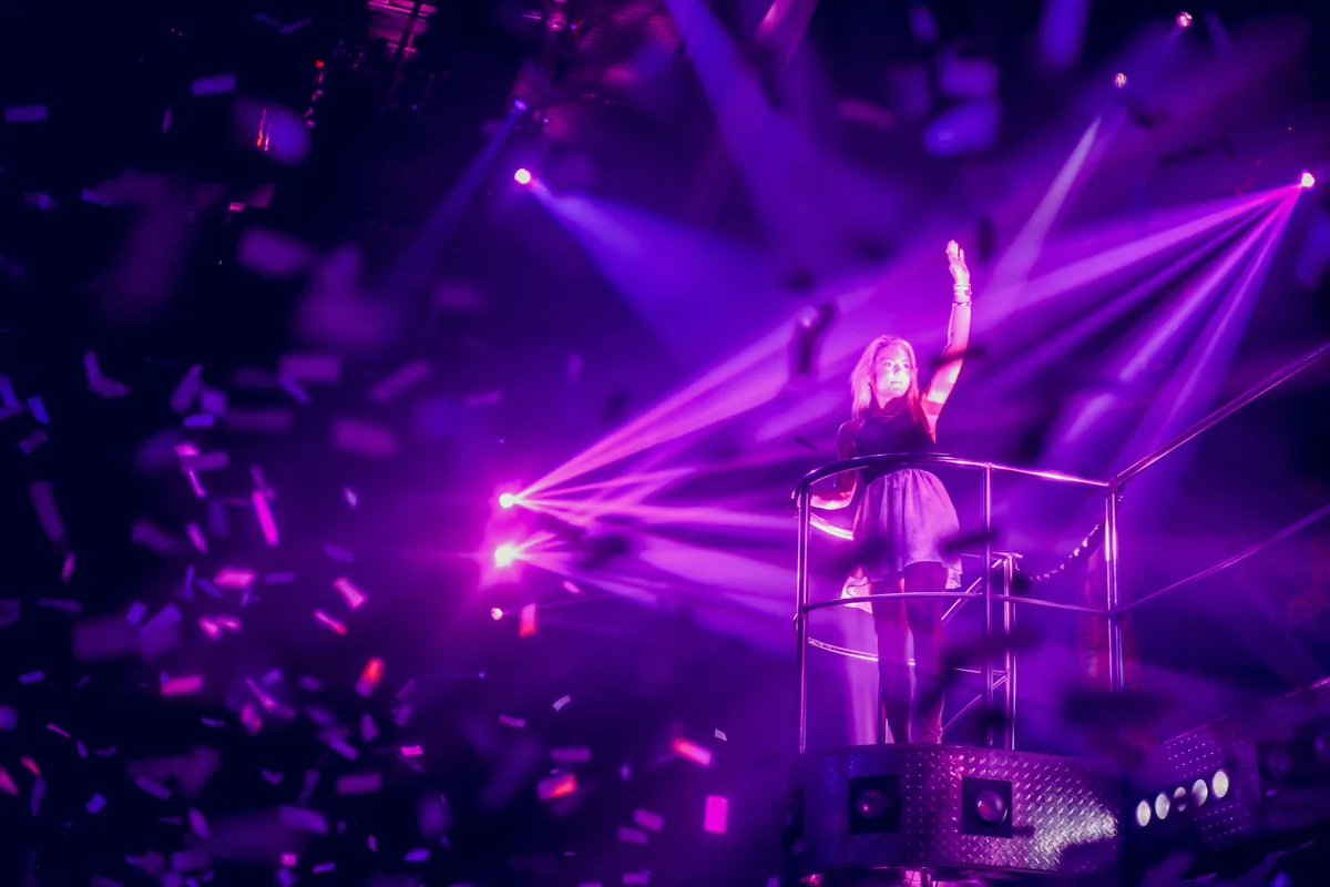 woman standing on a stage with purple lights from different directions all pointing at her.