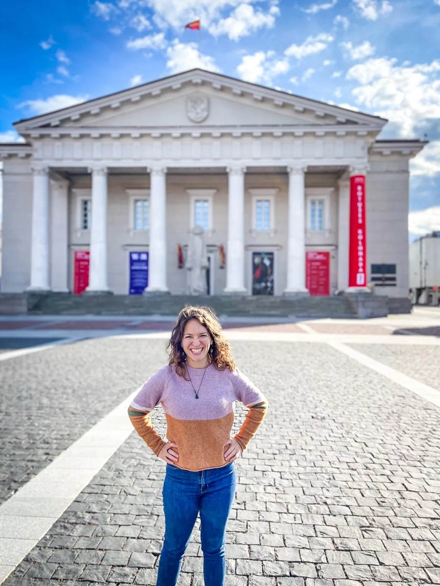 woman standing in front of town hall in Vilnius with blue skies above.