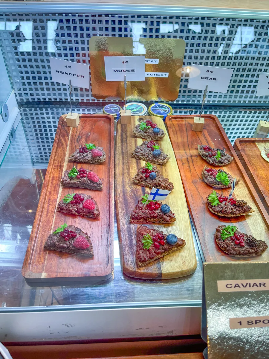 wooden chopping board topped with rows of toast topped with different meats and berries.