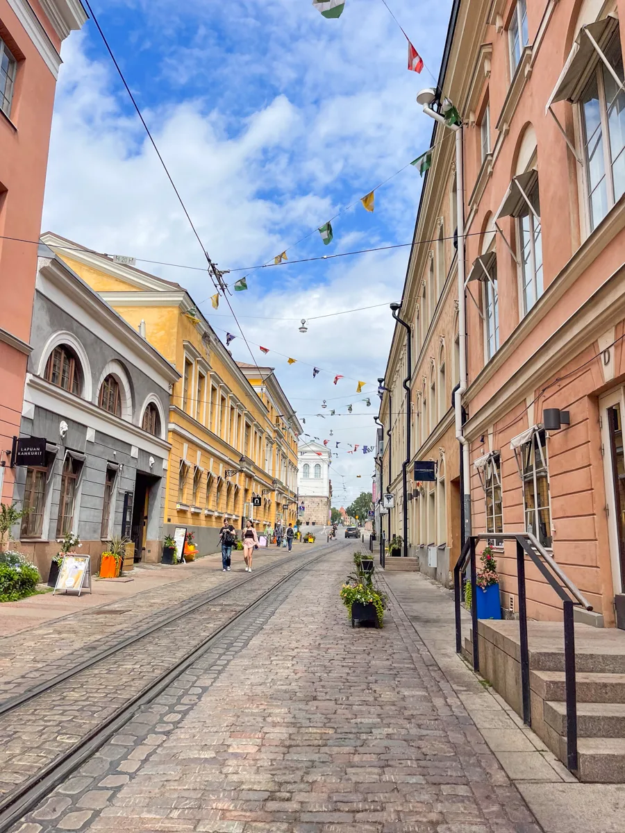 cobbled street with buildings on both sides and tram lines down the middle of the street with fabric triangle flags across the middle of the street.