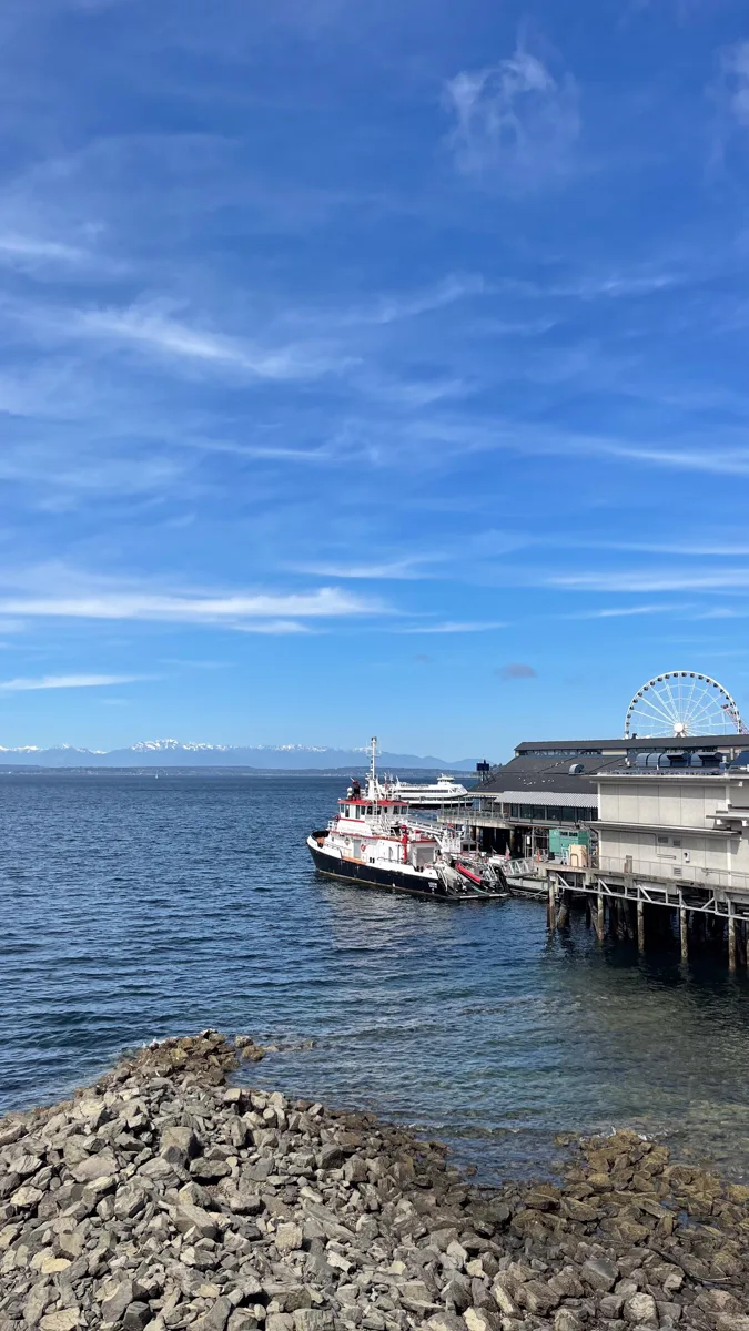 waterfront parea in Seattle with a small tugboat in the water and part of the ferris wheel in the distance to the right.