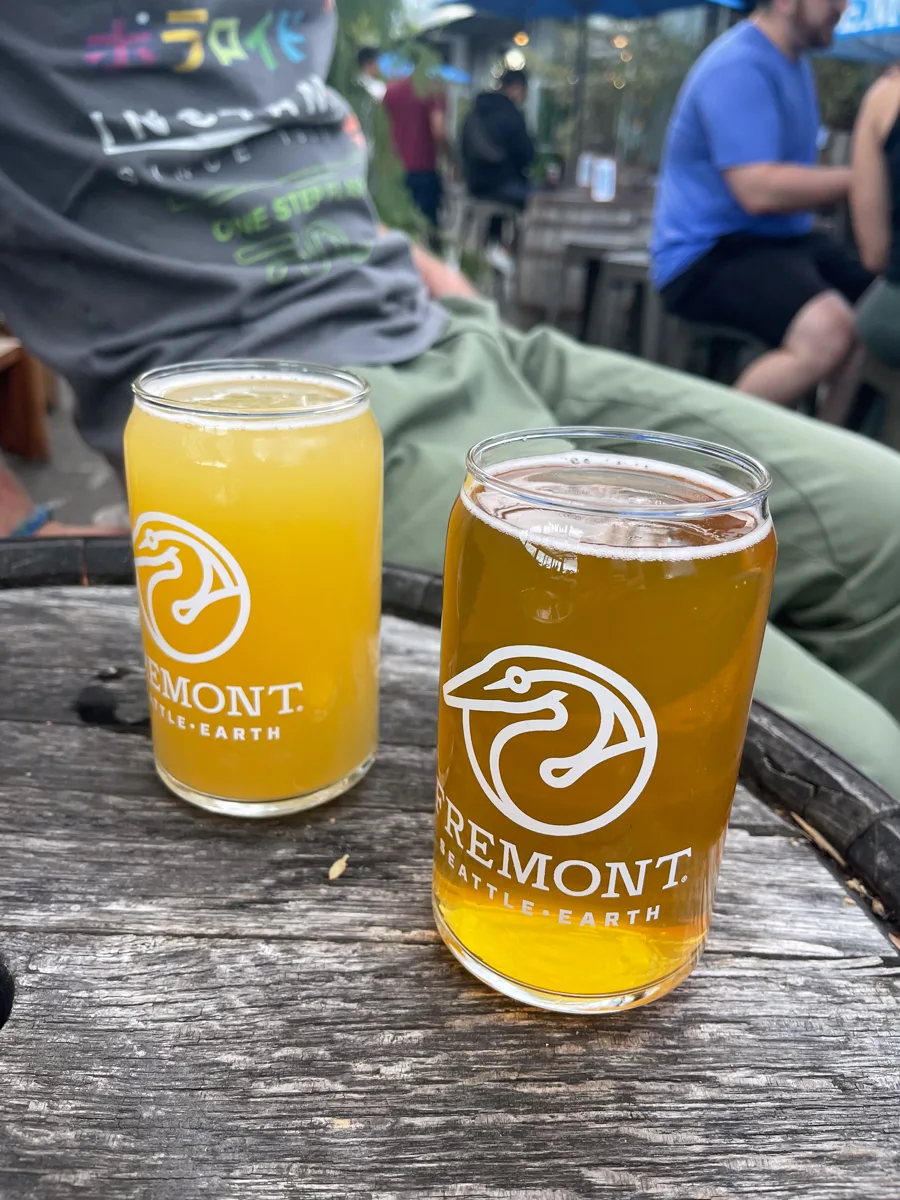 two beers from Fremont brewing, one is cloudy and one is clear, both are on top of a wooden barrel.