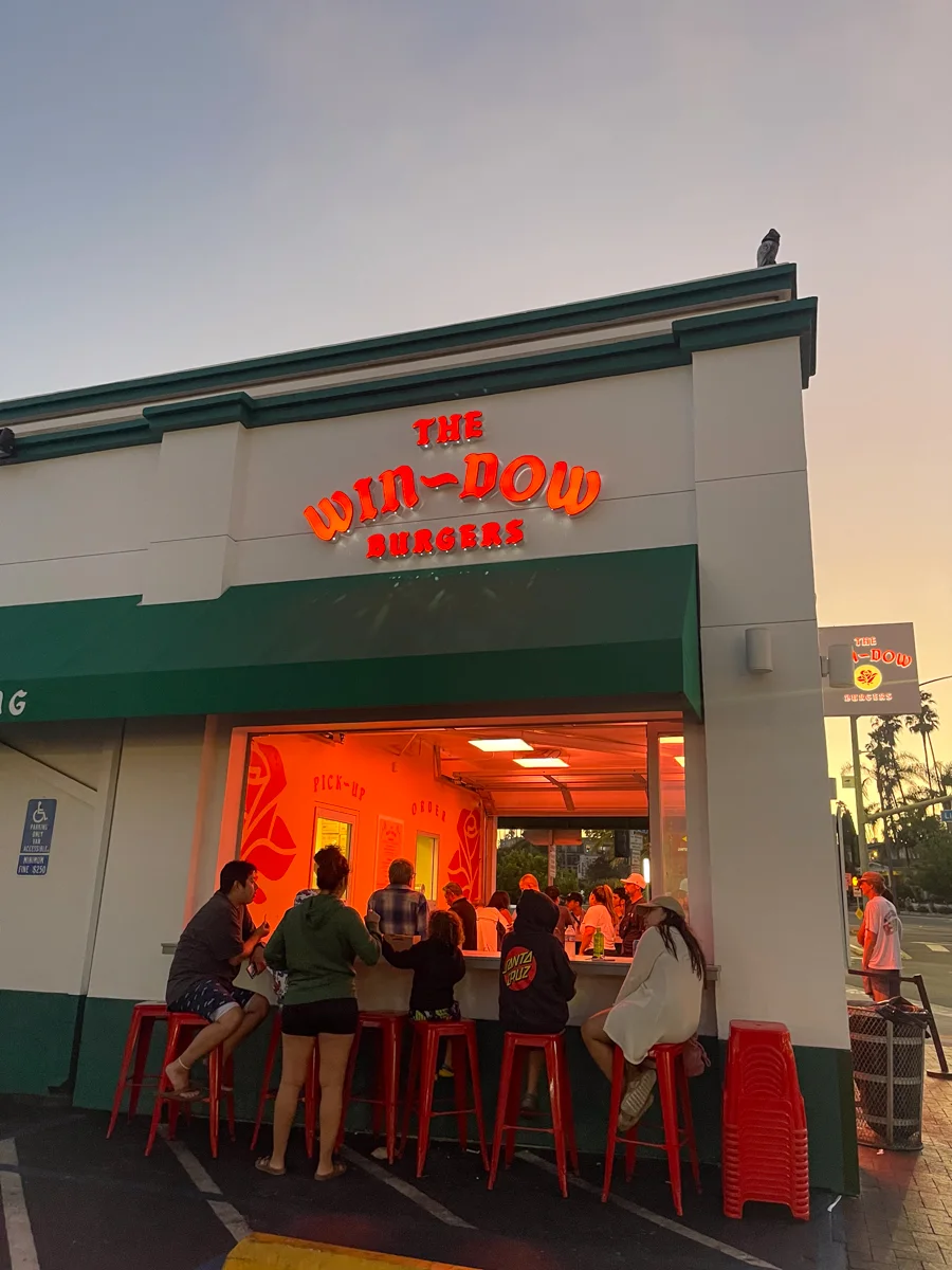 Front of a restaurant called the Win-Dow where people are lined up outside waiting to order.
