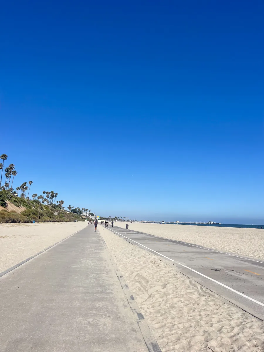 two concrete paths down the middle of a white sand beach with bright blue skies above, one of the best things to do in Long Beach is to ride along these paths in the sand.