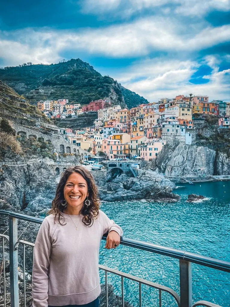 woman in a pink sweatshirt in front of a colorful town along the waterfront in Italy in October.