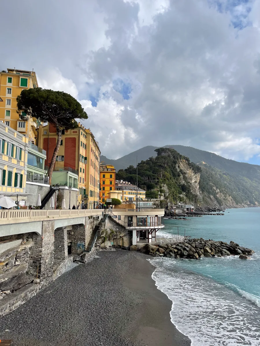 empty beach with clouds above and colorful buildings to the left of the shore.