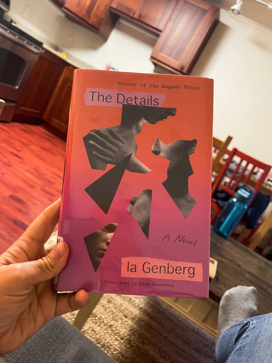holding up a book that says The Details with a small apartment in the background.