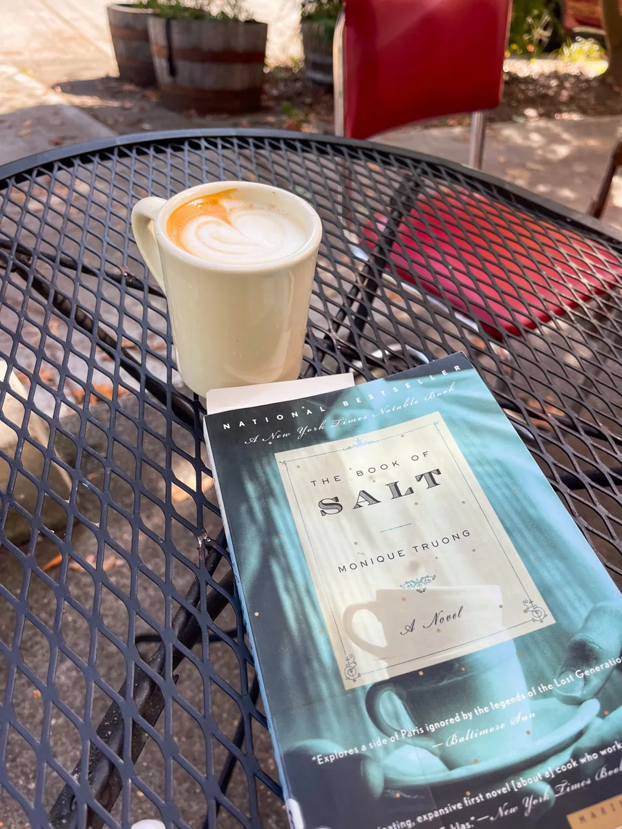 an outdoor table with a mug of coffee and a book sitting on top of the table.